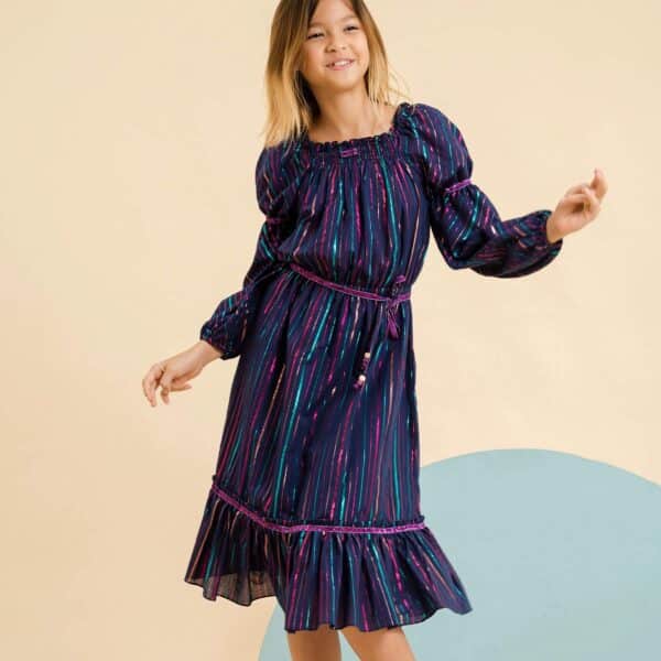 Long evening dress for little girls in indigo blue cotton with fine sequined stripes multicolored pink, green, purple. Collar smocks and puffy long sleeves with elastic at the wrists. Ruffles at the bottom of the dress. Details of purple ribbon with sequins at the bottom of the dress. Removable purple sequined belt, elastic waist. Fashion brand for children LA FAUTE A VOLTAIRE