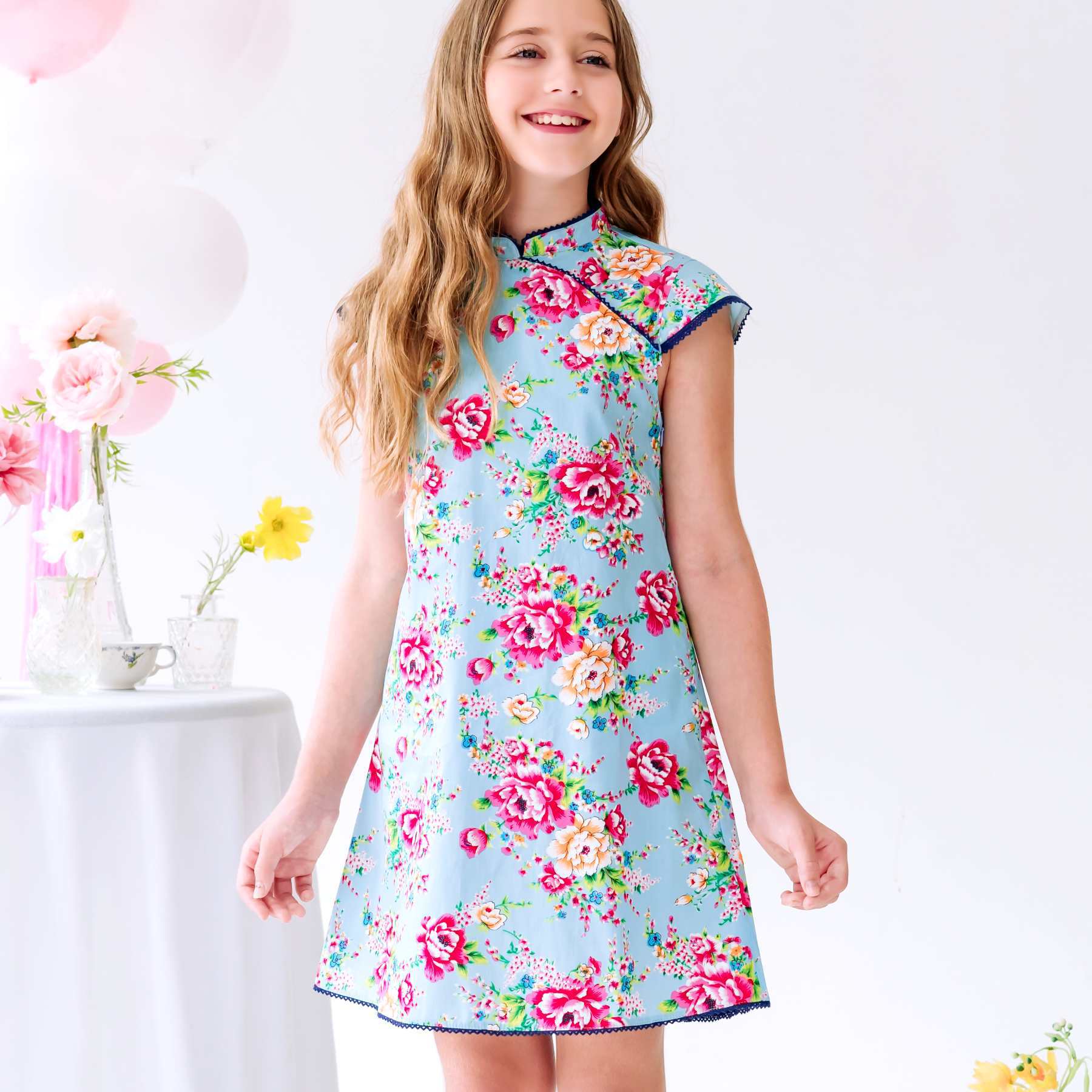 Photo portée robe Chinoise bleu turquoise fille fleurie rose fuchsia, avec Col Mao et Manches Courtes bordées de dentelle bleu marine. Idéale pour les cérémonies et mariages asiatiques élégants. Modèle Annam disponible de la taille 2 à 16 ans.