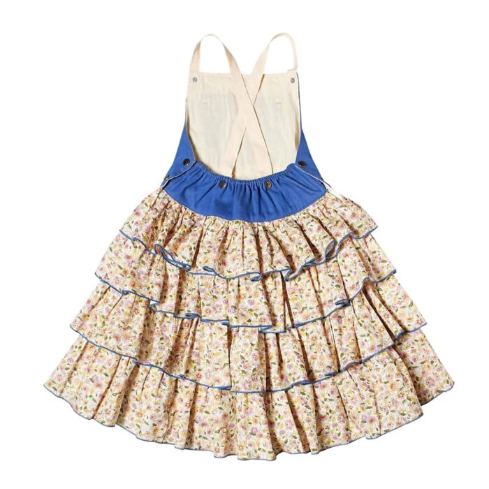 Girl's summer dungaree dress with blue denim cotton top and yellow and light blue floral ruffle bottom, adjustable cross-back straps. Model dungarees dress with ruffles for girls, girls of the brand of children's fashion LA. FAUTE A VOLTAIRE