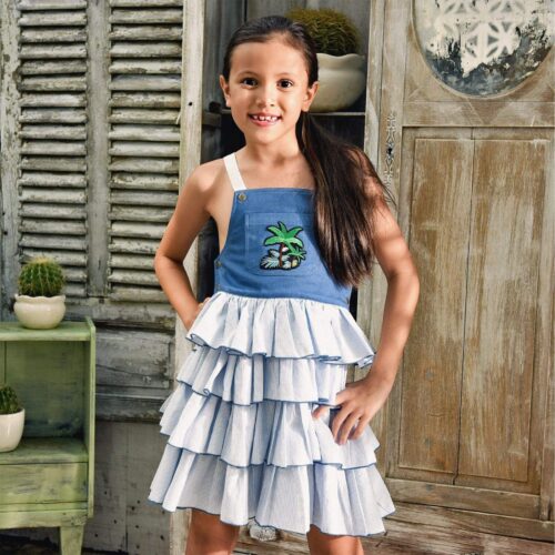 Girl's summer dungaree dress with beige cotton denim top and light blue and white striped ruffled bottom with adjustable cross-back straps. Ruffled overalls dress for girls of the children's fashion brand LA FAUTE A VOLTAIRE