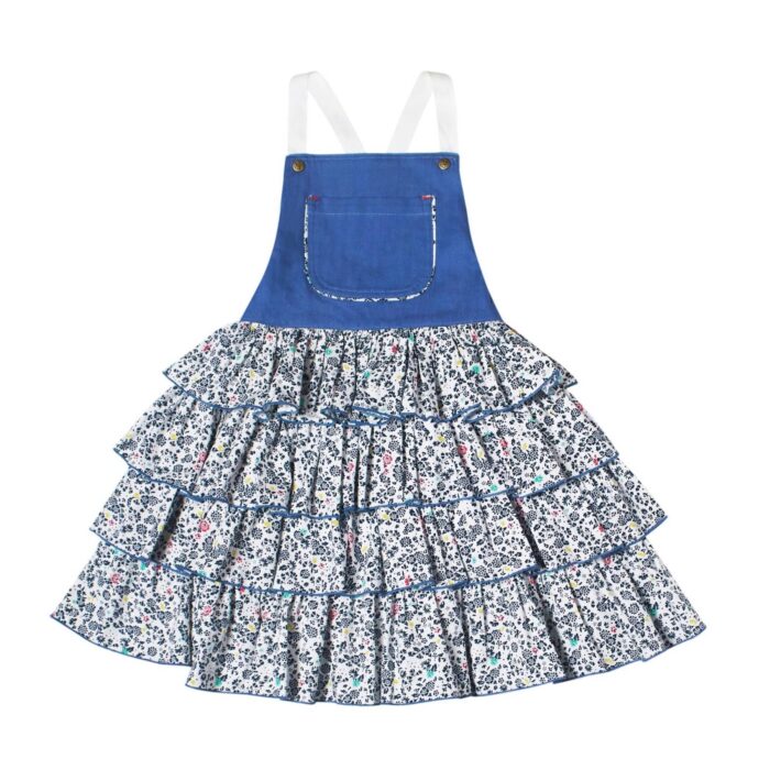 Girl's summer dungaree dress with blue denim cotton top and navy, red, white floral ruffle bottom with adjustable cross back straps. Model dungarees dress with ruffles for girls, girls of the brand of children's fashion LA. FAUTE A VOLTAIRE