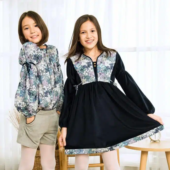 On Craque pour cette Élégante et Originale Robe d'Hiver pour Fille en Velours Millerais Bleu Marine et plastron matelassé en Fleuri Liberty Violet et Lilas de la Marque de Mode pour Enfant La Faute à Voltaire.