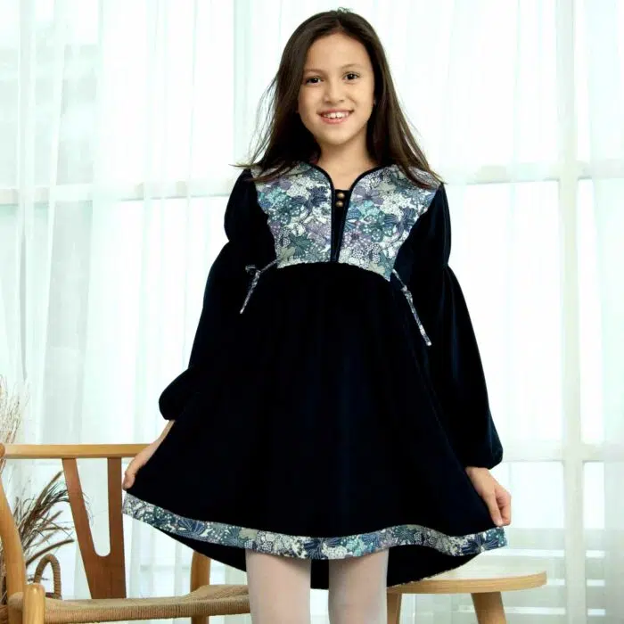 On Craque pour cette Élégante et Originale Robe d'Hiver pour Fille en Velours Millerais Bleu Marine et plastron matelassé en Fleuri Liberty Violet et Lilas de la Marque de Mode pour Enfant La Faute à Voltaire.