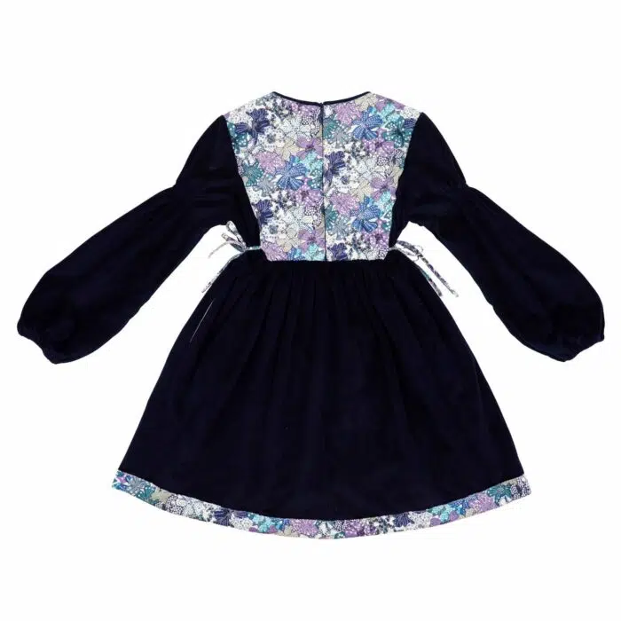 On Craque pour cette Élégante et Originale Robe d'Hiver pour Fille en Velours Millerais Bleu Marine et plastron matelassé en Fleuri Liberty Violet et Lilas de la Marque de Mode pour Enfant La Faute à Voltaire.