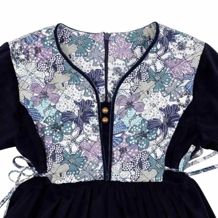 On Craque pour cette Élégante et Originale Robe d'Hiver pour Fille en Velours Millerais Bleu Marine et plastron matelassé en Fleuri Liberty Violet et Lilas de la Marque de Mode pour Enfant La Faute à Voltaire.