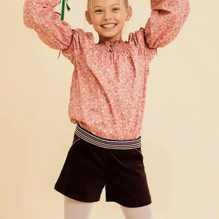 Short hiver fille en velours bordeaux, prune et ceinture intégrée à paillettes multicolore rose, or, bleu et violet. Taille ajustable avec élastique dans le dos, poches surlignées d'un biais rose à paillettes, ouverture sur le côté avec fermeture éclair et bouton pression. LA FAUTE A VOLTAIRE, marque de vêtement enfant en commerce équitable