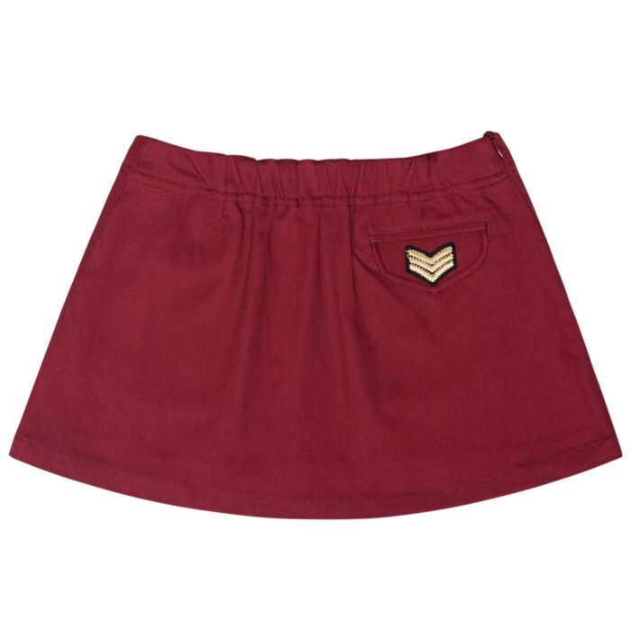 Short skirt in burgundy plum cotton, trapeze shape, adjustable waist with elastic in the back, pink flower patch on the front. Children's fashion clothing from the French fair trade brand LA FAUTE A VOLTAIRE