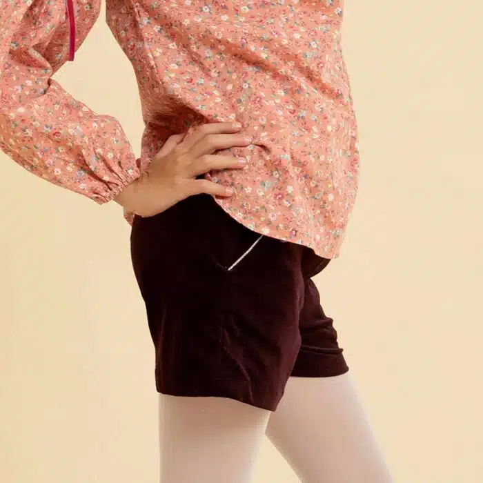 Short hiver fille en velours bordeaux, prune et ceinture intégrée à paillettes multicolore rose, or, bleu et violet. Taille ajustable avec élastique dans le dos, poches surlignées d'un biais rose à paillettes, ouverture sur le côté avec fermeture éclair et bouton pression. LA FAUTE A VOLTAIRE, marque de vêtement enfant en commerce équitable