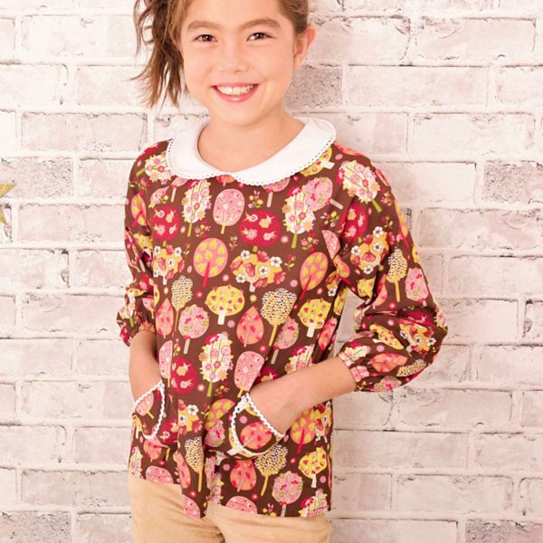 little girl's blouse in brown cotton with pink, yellow and green tree print. With white Claudine collar edged with white lace, small rounded pockets on the front. Blouse model Claudine of the brand LA FAUTE A VOLTAIRE