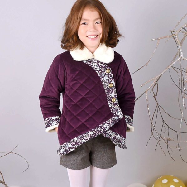 Short and warm coat for girls in velvet ras burgundy plum quilted kimono shape with contrasting band in floral fabric liberty purple and pink, closure with large buttons bronze color, beige faux fur collar. Retro-chic fair trade children's clothing brand LA FAUTE A VOLTAIRE