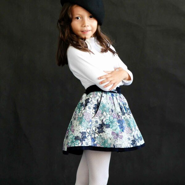 Pretty skirt trendy winter girl in cotton flowered liberty navy blue, purple, lilac. Elastic belt in navy blue velvet, pockets lined with velvet and small decorative bow on the belt. Children's fashion brand in fair trade LA FAUTE A VOLTAIRE.