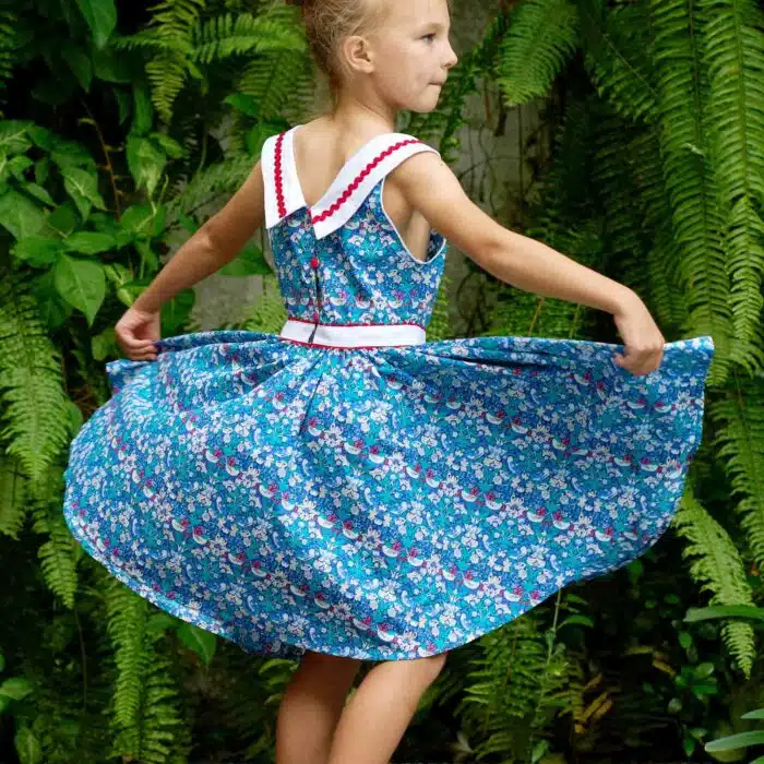 Elégante robe qui tourne à l'horizontal à l'imprimé floral et oiseaux bleu marine, vert et rouge, large col bateau blanc avec dentelle en zigzag rouge, ceinture blanche, emmanchure américaine pour filles de 2 à16 ans de la marque de mode pour enfants LA FAUTE A VOLTAIRE