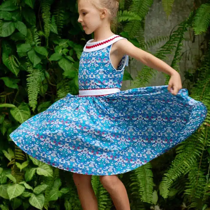 Pour un mariage rétro-chic, une fête estivale, on craque pour cette élégante robe d'été qui tourne à l'horizontal à l'imprimé floral et oiseaux bleu marine, vert et rouge, large col bateau blanc avec dentelle en zigzag rouge, ceinture blanche, emmanchure américaine pour filles de 2 à16 ans de la marque de mode pour enfants LA FAUTE A VOLTAIRE