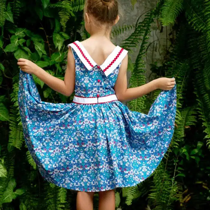 Pour un mariage rétro-chic, une fête estivale, on craque pour cette élégante robe d'été qui tourne à l'horizontal à l'imprimé floral et oiseaux bleu marine, vert et rouge, large col bateau blanc avec dentelle en zigzag rouge, ceinture blanche, emmanchure américaine pour filles de 2 à16 ans de la marque de mode pour enfants LA FAUTE A VOLTAIRE