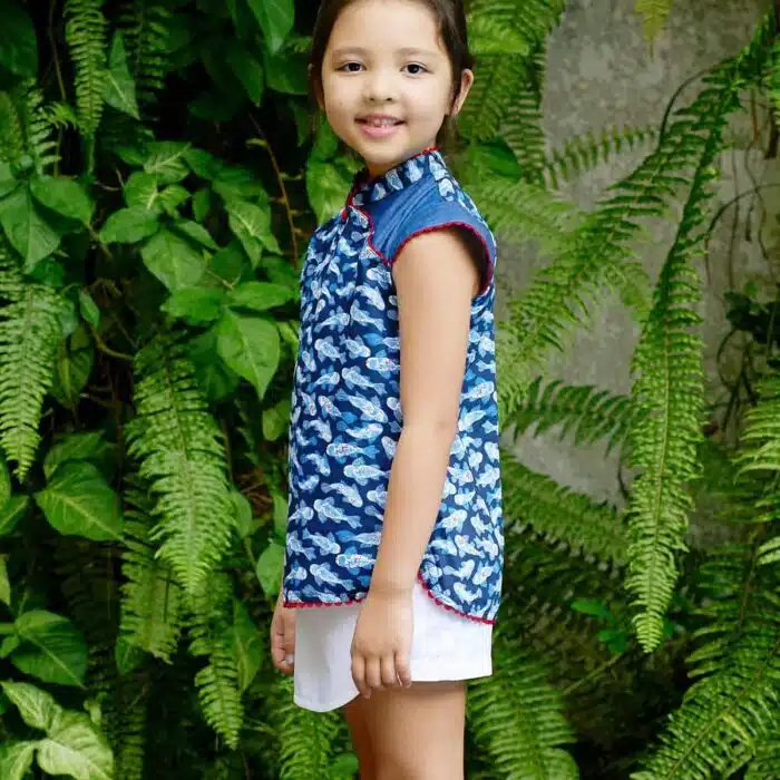 Blouse chinoise en coton imprimé poissons Khoi bleu marine, bleu clair et rouge. Les manches courtes coupées en biais, le col Mao et le bord de la blouse bordée de biais rouge. Blouse asiatique pour filles, fillettes et ados de la marque de mode pour enfants LA FAUTE A VOLTAIRE