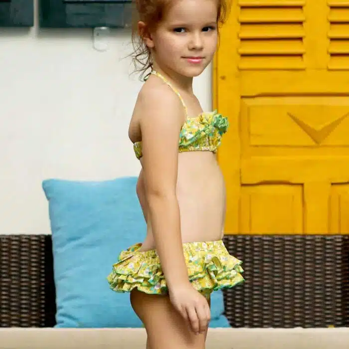 Maillot de bain deux pièces à volants en coton fleuri jaune et vert. Haut du maillot forme bandeau à volant avec élastique dans le dos et bas du maillot coupe taille basse à volants. Maillot de bain deux pièces pour filles, fillettes et ados de la marque de mode pour enfant LA FAUTE A VOLTAIRE