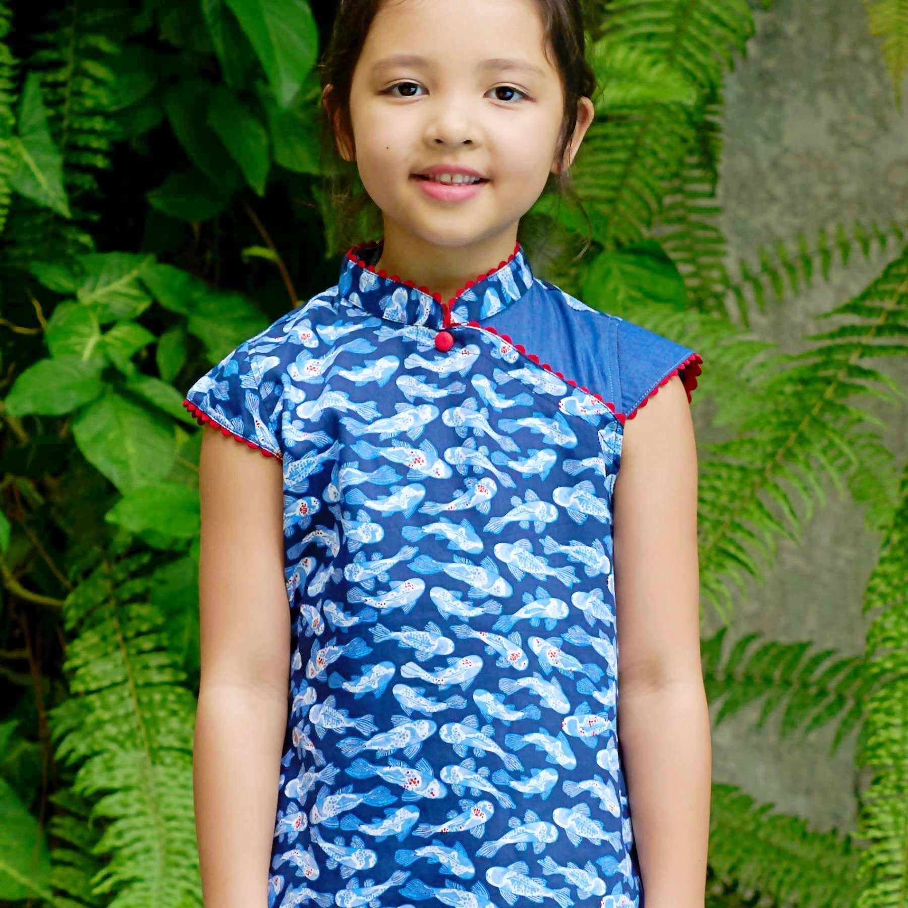 Craquez pour cette adorable robe chinoise pour filles, fillettes et ados en coton imprimé poisson carpes japonais bleu marine, bleu ciel, blanc et rouge. Le col Mao, les manches courtes coupées en biais et le bas de la robe sont contrastées d'un biais de dentelle de forme arrondie couleur rouge qui apporte délicatesse et fantaisie à cette jolie robe asiatique de la marque de mode pour enfants La Faute à Voltaire