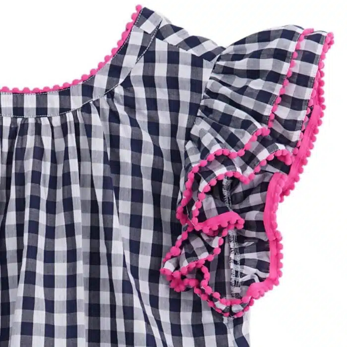 Jolie robe à carreaux vichy bleu marine et blanc, à manches papillons à volants, col rond devant et col V dans la nuque, rangée de pompons rose fuchsia autour des volants, col et bas de la robe. Robe été pour filles, fillettes et ados de la marque de mode pour enfants La Faute à Voltaire