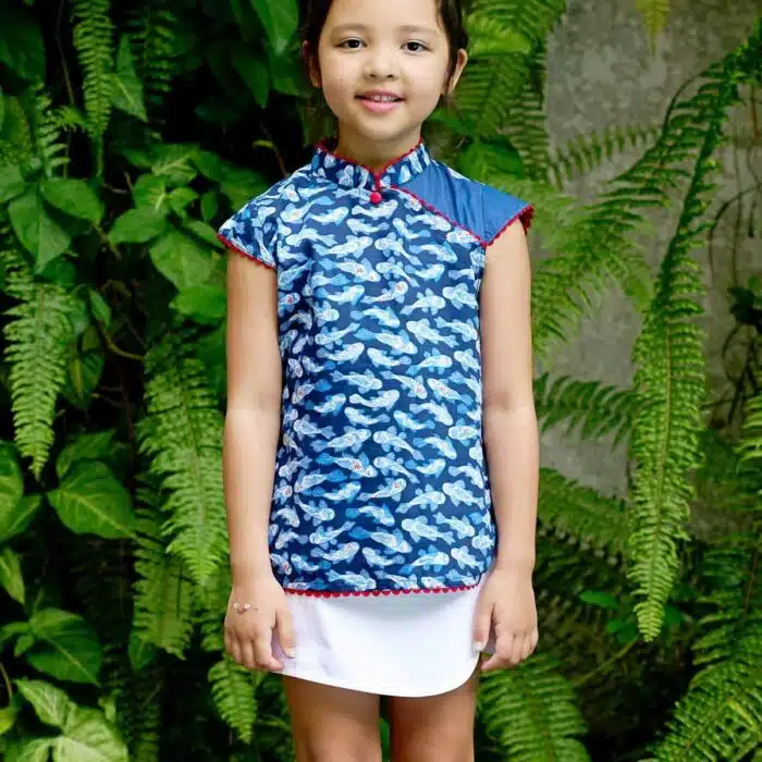 Blouse chinoise en coton imprimé poissons Khoi bleu marine, bleu clair et rouge. Les manches courtes coupées en biais, le col Mao et le bord de la blouse bordée de biais rouge. Blouse asiatique pour filles, fillettes et ados de la marque de mode pour enfants LA FAUTE A VOLTAIRE