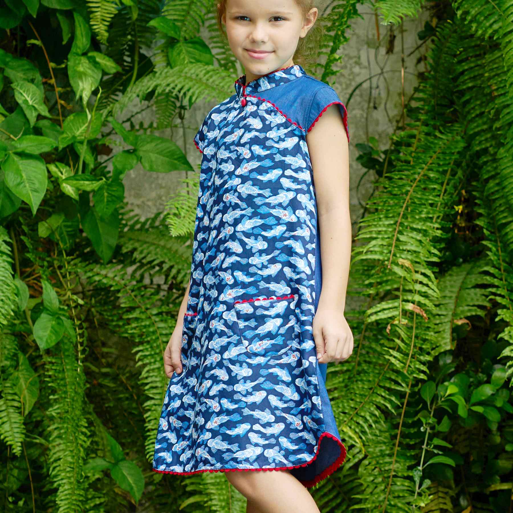 Craquez pour cette adorable robe chinoise pour filles, fillettes et ados en coton imprimé poisson carpes japonais bleu marine, bleu ciel, blanc et rouge. Le col Mao, les manches courtes coupées en biais et le bas de la robe sont contrastées d'un biais de dentelle de forme arrondie couleur rouge qui apporte délicatesse et fantaisie à cette jolie robe asiatique de la marque de mode pour enfants La Faute à Voltaire