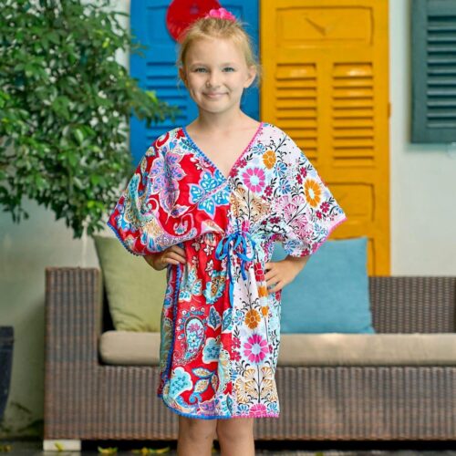 Jolie robe tunique de plage ample avec un lien ajustable à la taille, en coton fleurs hawaÏ blanc et rose à droite et rouge fleurs hawaï bleu à gauche. Col V devant et dans la nuque bordée de pompons rose et bleu. Robe de plage pour filles, fillettes et ados de la marque de mode pour LA FAUTE A VOLTAIRE
