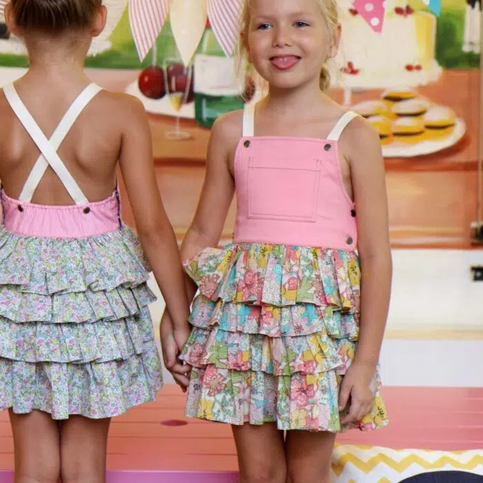 Une adorable Robe Salopette Printemps été pour Fille avec Plastron avant en Coton Rose et jupe à volants fleuris liberty dans les tons abricot, jaune, vert. Bretelles croisées dans le dos. Ouverture avec boutons pressions dans sur les côtés. Modèle de la marque de mode pour enfants LA FAUTE A VOLTAIRE.