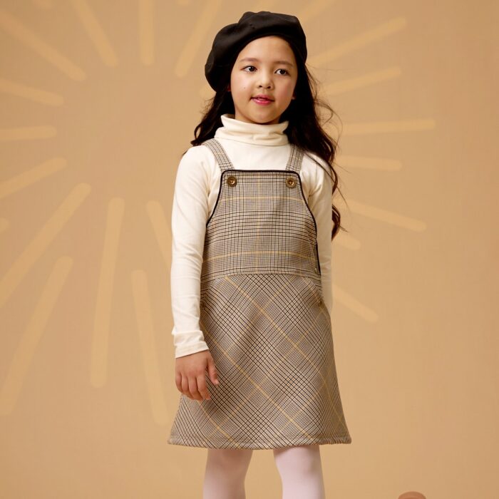 Somptueux ensemble d'hiver composé d'une robe salopette au style écolier en carreaux tartan jaune et marron, avec un pull col roulé beige tout doux de la marque de mode française pour enfants LA FAUTE A VOLTAIRE