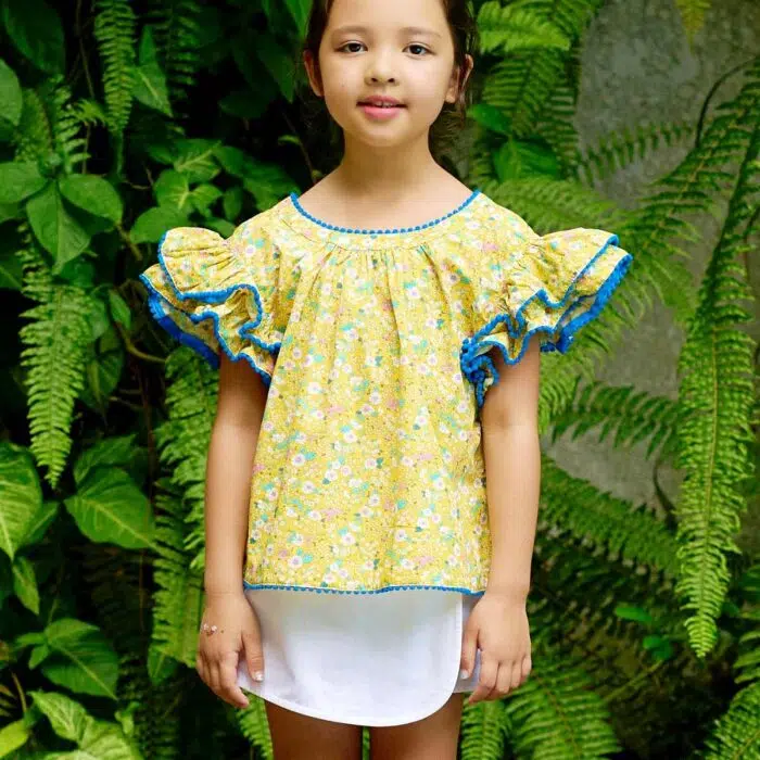 Laissez-vous séduire par l'éclat de notre ensemble estival, où le jaune ensoleillé de la blouse se marie à la pureté du blanc de la jupe-short. La blouse, avec ses manches papillon à double rangée de volants et ses pompons bleu foncé, apporte une touche d'originalité et de fantaisie. Son col rond à l'avant et son col V à l'arrière ajoutent une note de raffinement. Confortable et légère, cette blouse est idéale pour les journées chaudes. La jupe-short, quant à elle, offre une liberté de mouvement optimale pour toutes les activités estivales de votre petite princesse. Un ensemble parfait pour un été plein de style et de joie !