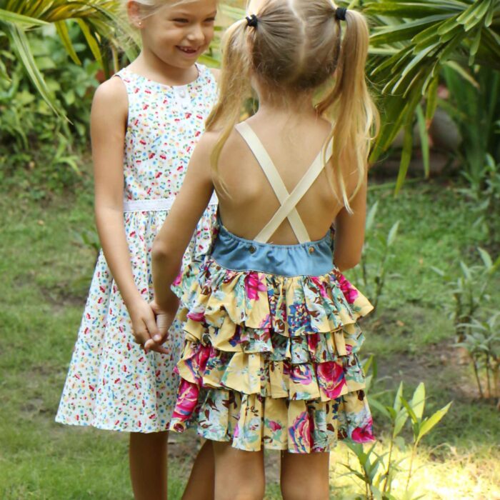 Robe salopette été fille avec haut en coton jean denim bleu et bas de la robe à volants fleurie jaune et multicolor, bretelles croisées dans le dos ajustables. Modèle robe salopette à volants pour filles, fillettes de la marque de mode enfant LA FAUTE A VOLTAIRE