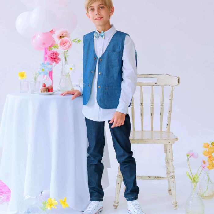 Une élégante Tenue de Mariage pour Enfant avec un Pantalon Jeans Denim Coupe Slim Fit Couleur Bleu Foncé, une Chemise Blanche à Col Pointu, un Gilet de Costume Bleu Foncé assorti au Jeans et un Adorable Nœud Papillon en Coton Fleuri Liberty bleu. Collection Cérémonie Mode Enfant de la Marque de Mode Chic et Tendance Française La Faute à Voltaire.
