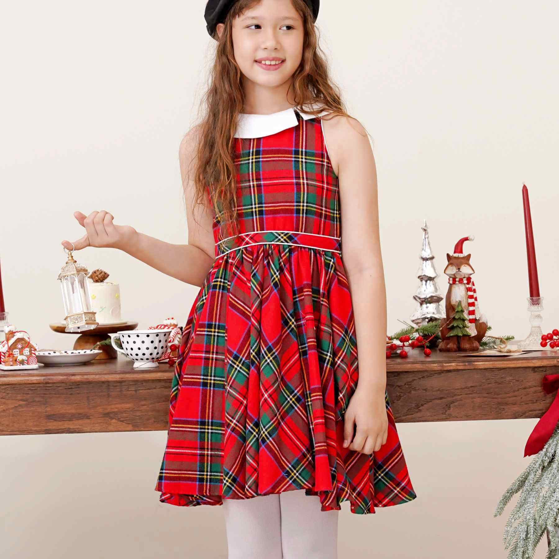 Une Élégante Robe Patineuse qui Tourne en Flanelle Carreaux Tartan Rouge et Vert, sans Manche, Col Claudine Blanc Tourné sur le Côté, Taille Marquée par Deux Biais de Coton Blanc, Emmanchures Américaines. Pour les Fêtes de Noël et Tous les Jours de l'Automne et Hiver. A porter avec des Collants Fins Blanc et un Gilet Blanc. Marque de Mode Rétro-Chic et Commerce Équitable de la Marque de Mode pour Enfant La Faute à Voltaire.