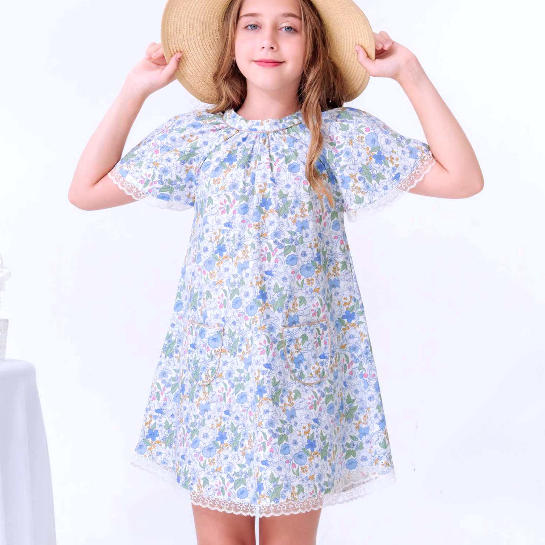 Photo portée de la robe de demoiselle d'honneur fleurie liberty bleu pastel et rose pour fille. Robe de cérémonie coupe A, col, rond bordé d'un biais doré, manches papillon bordées de fine dentelle anglaise beige mordoré. Modèle robe d'été Butterfly disponible de 2 à 16 ans de la marque de mode pour enfants La Faute à Voltaire.