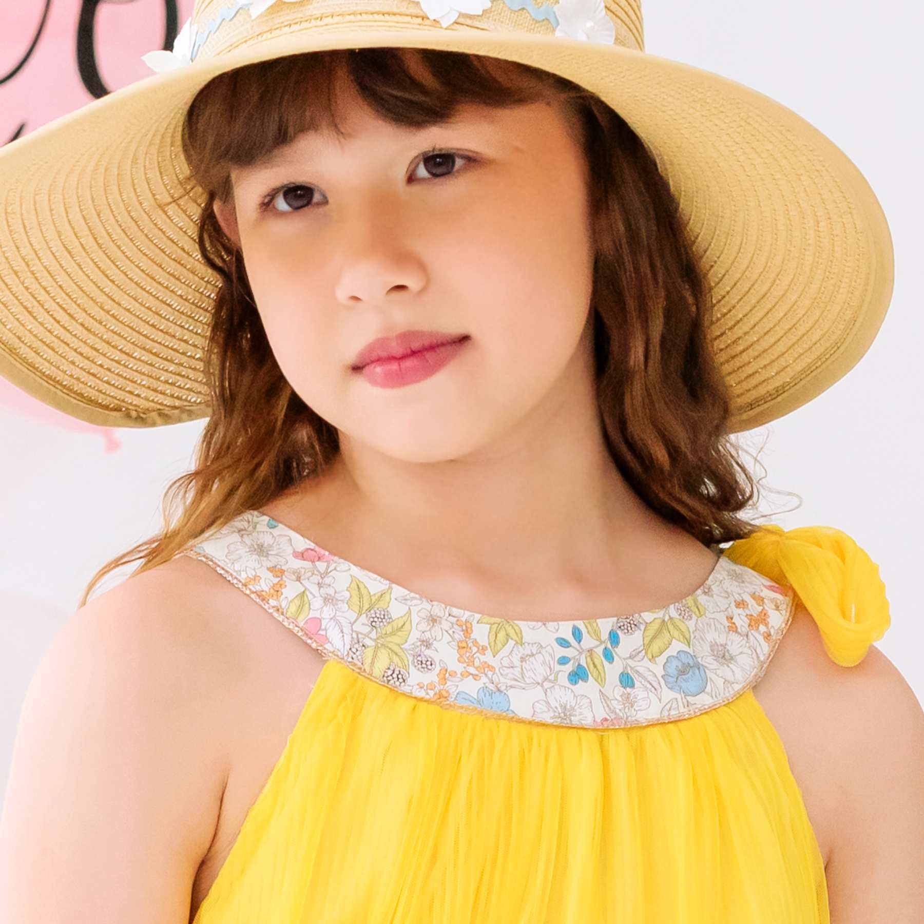 Photo portée en gros plan du col fleuri liberty rose, bleu, vert de la robe de demoiselle d'honneur Alizée en voile jaune pour fille. modèle disponible du 2 au 16 ans.