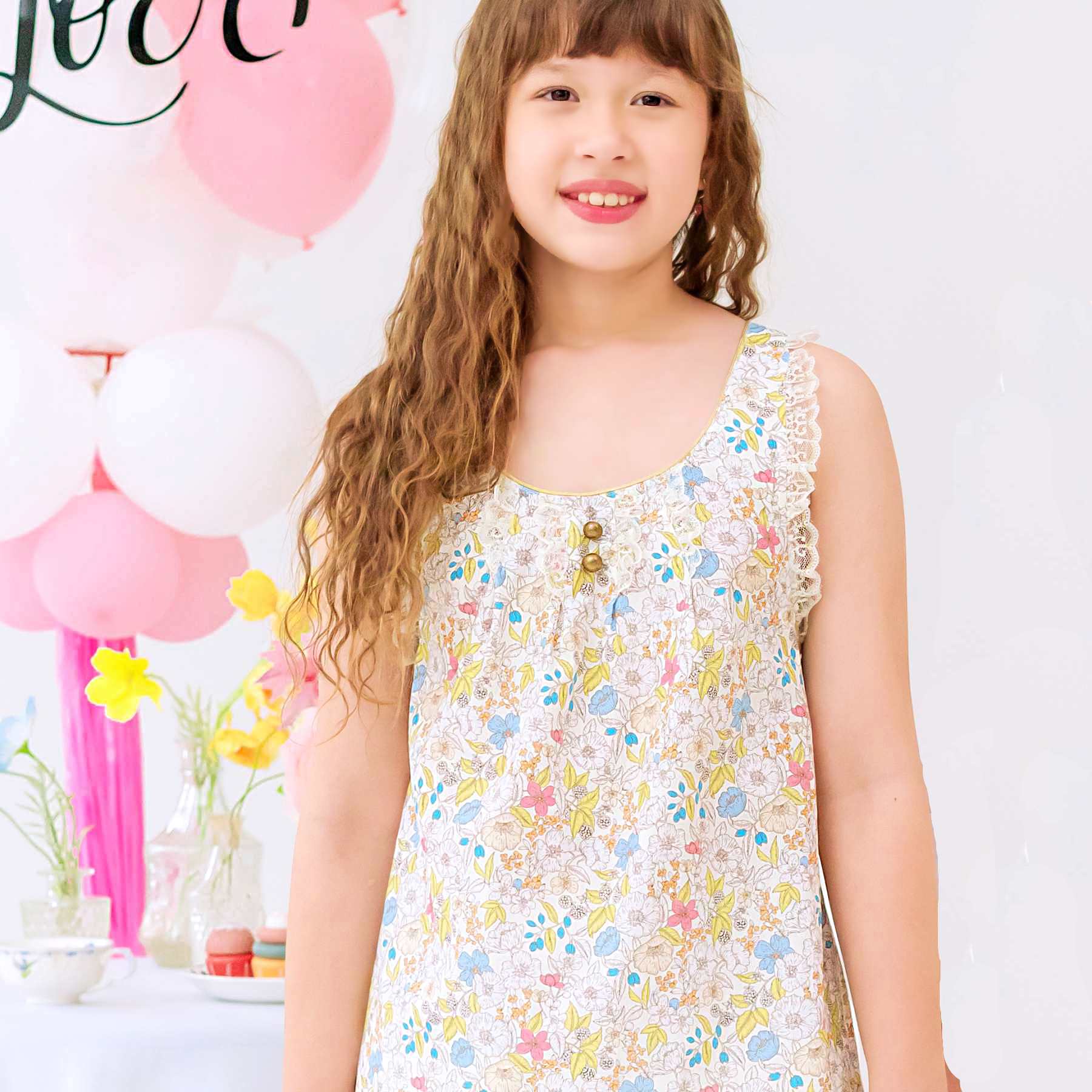 Photo portée de la robe de cérémonie fille fleurie liberty jaune pale ANAÏS avec bretelles croisées bordées de fine dentelle beige mordoré, poches bordées d'un biais doré. Tenue de mariage bohème chic ou robe d'été élégante, disponible du 2 au 16 ans.