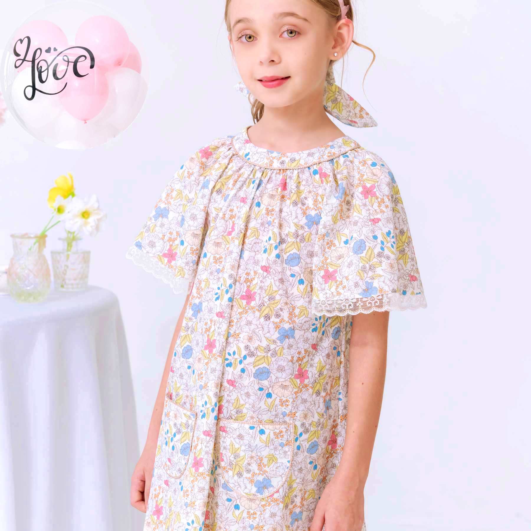 Photo gros plan portée de la robe de cérémonie fleurie liberty jaune pastel et rose pour fille. Robe de cérémonie coupe A, col, rond bordé d'un biais doré, manches papillon bordées de fine dentelle anglaise beige mordoré. Modèle robe d'été Butterfly disponible de 2 à 16 ans de la marque de mode pour enfants La Faute à Voltaire.