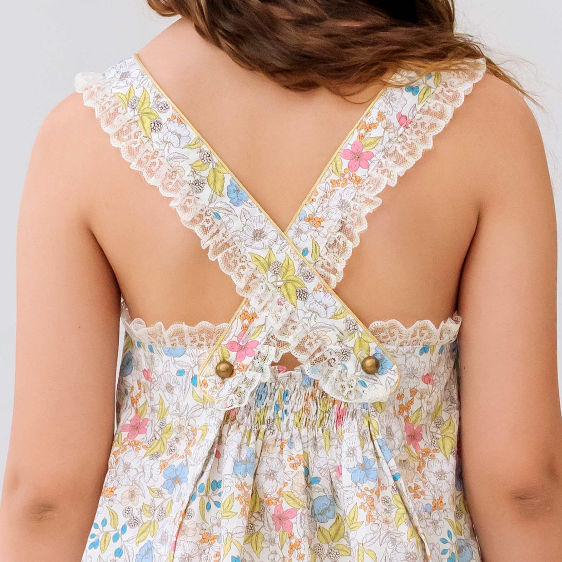 Photo porté en gros plan du dos de la robe de cérémonie fille liberty jaune pale ANAÏS à col rond, bretelles bordées de fine dentelle beige mordoré, deux boutons couleur bronze décoratif. Tenue de mariage bohème chic ou robe d'été élégante, disponible du 2 au 16 ans.