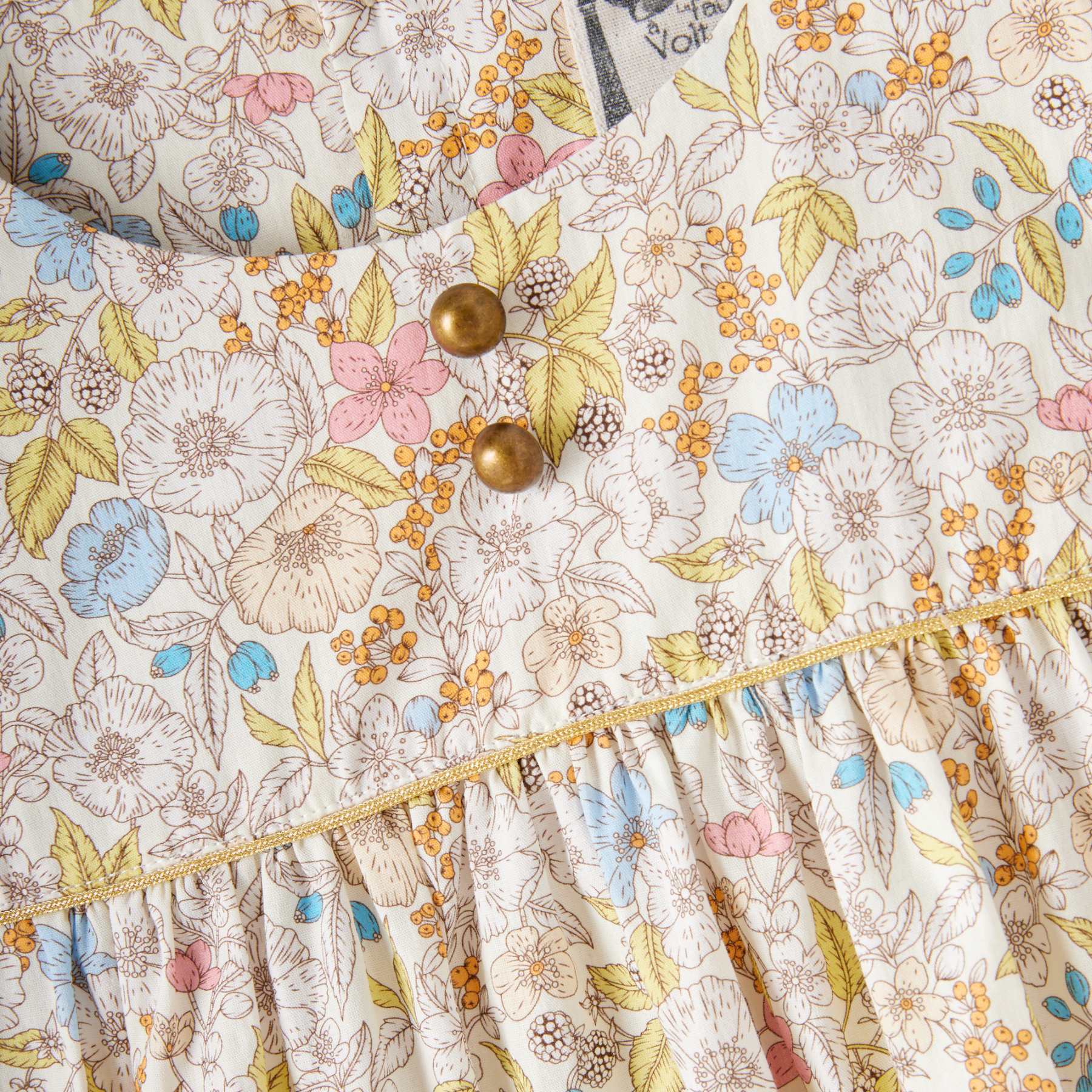 photo packshot zoom de du plastron avant de la robe de cérémonie fille fleurie liberty jaune, rose, bleu ciel avec petits boutons ronds couleur bronze décoratif, biais doré sur la poitrine. Robe idéale pour demoiselle d'honneur, mariage bohème chic et tous les évènements chics de l'été. Disponible du 2 au 16 ans.