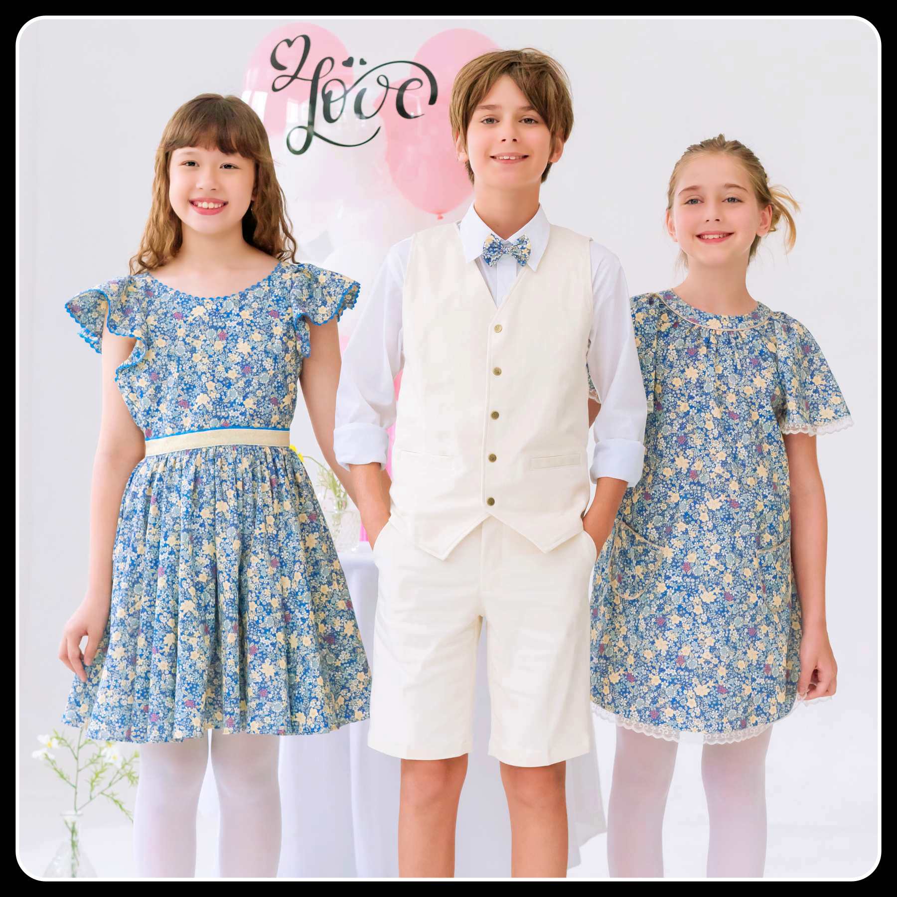 Photo tenues de cérémonie enfant portées par un garçon avec gilet de costume et bermuda beige, chemise blanche et noeud papillon liberty bleu, une robe manches courtes à volants en liberty bleu et détails doré, une robe manches papillon fleurie liberty bleu foncé et fine dentelle beige mordoré.