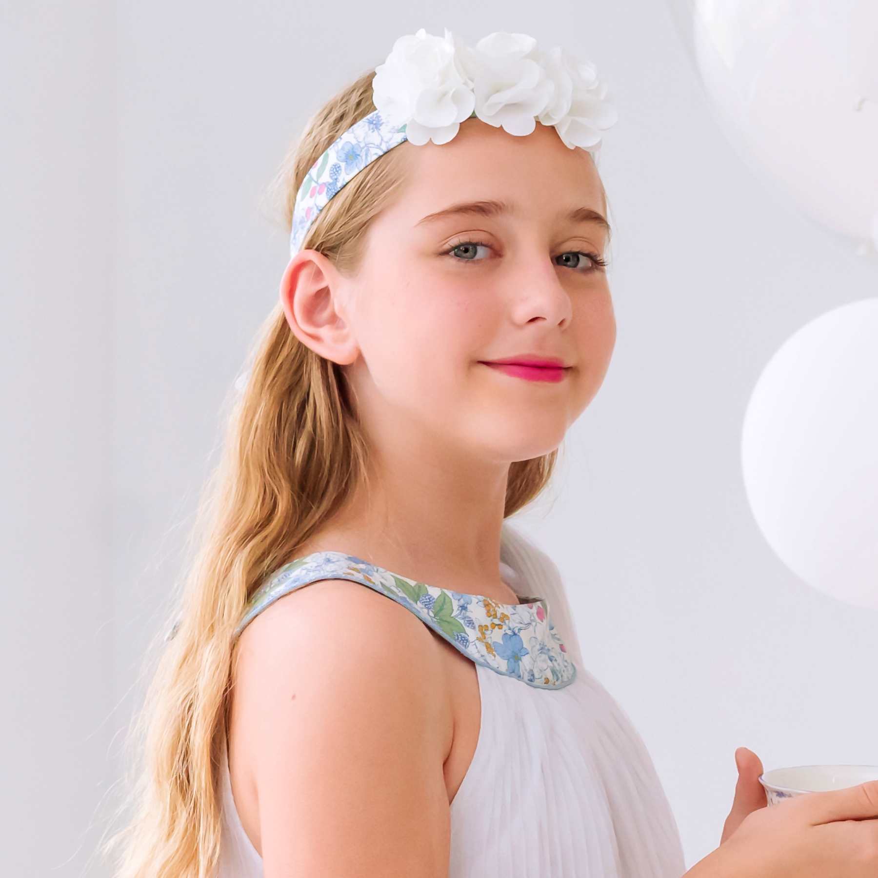 Bandeau cheveux fille cérémonie fleuri bleu ciel avec fleurs blanches délicates sur l'avant, élastique doré pour un maintien parfait. Disponible du 2 au 16 ans.