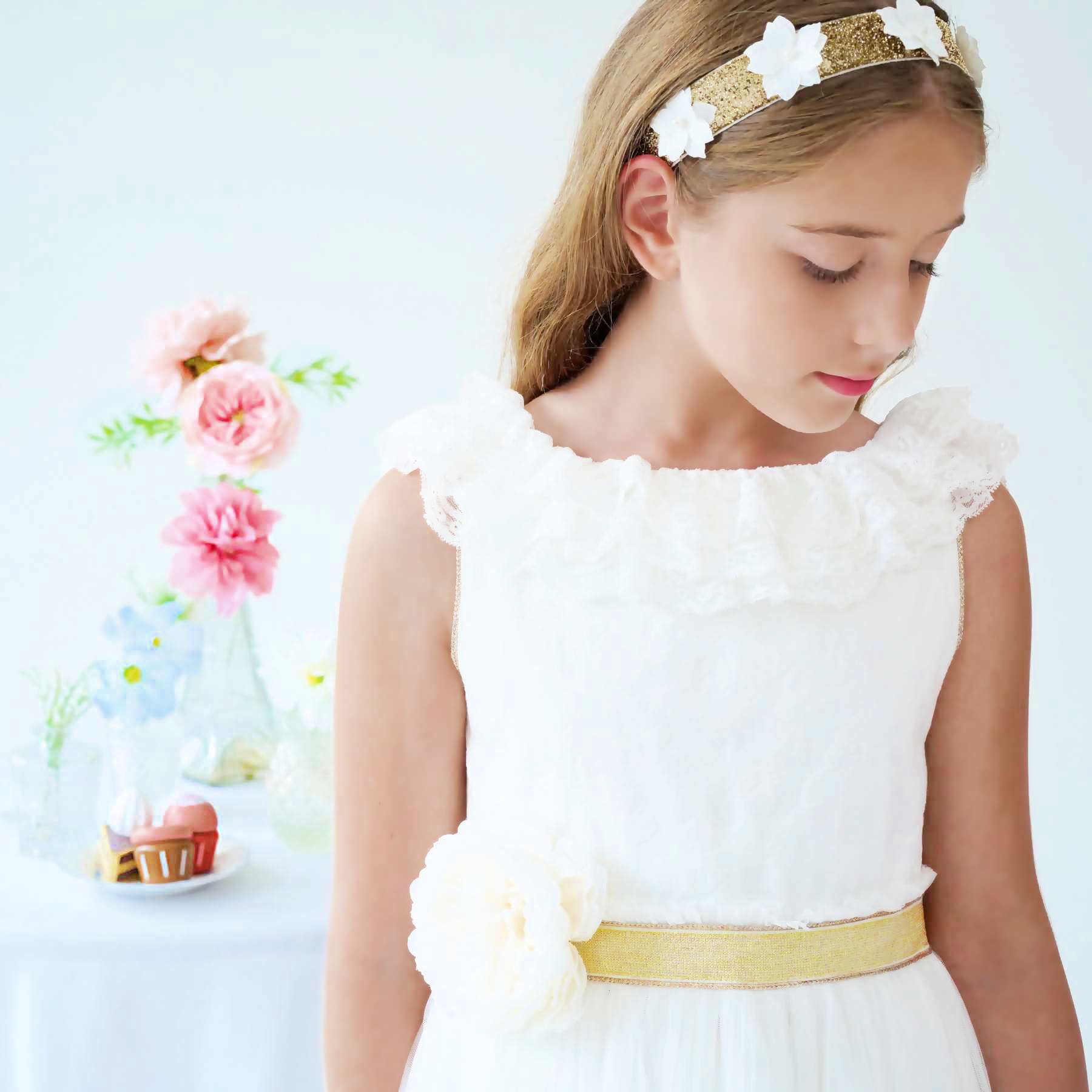 Bandeau cheveux fille cérémonie doré avec fleurs blanches brodées. Ruban en dentelle beige à nouer derrière la nuque. Idéale avec la robe de demoiselle d'honneur Éléonaure.