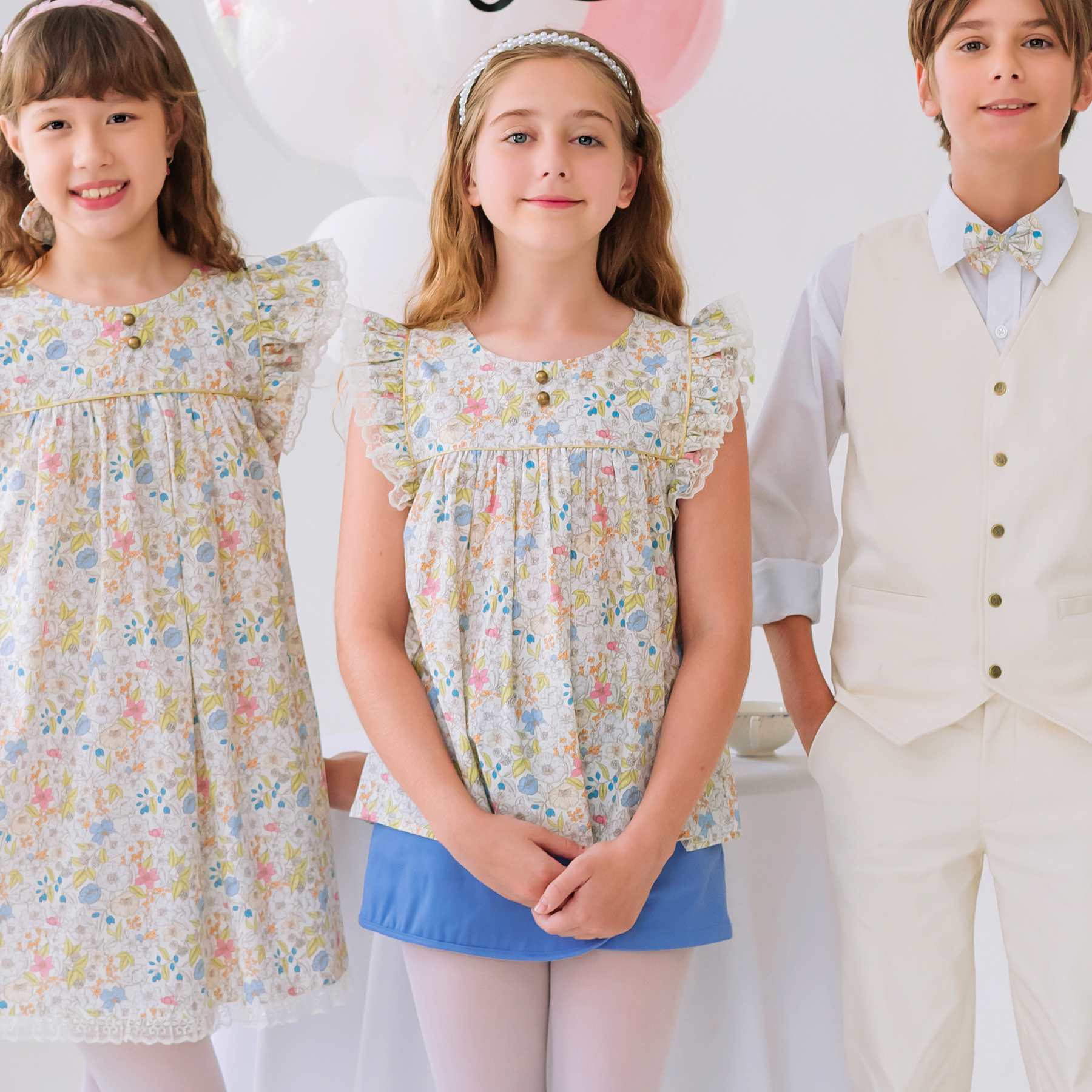 Photo portée de la blouse fleurie fille liberty jaune, rose, bleu pastel avec manches courtes à volants bordées de fine dentelle beige, biais et petits boutons dorés sur le devant. Modèle idéale pour tous les jours mais aussi pour une cérémonie estivale. Parfaite avec la jupe short Jade bleu. Disponible de la taille 2 à 16 ans. Cette blouse taille normalement, prenez la taille habituelle de votre enfant.