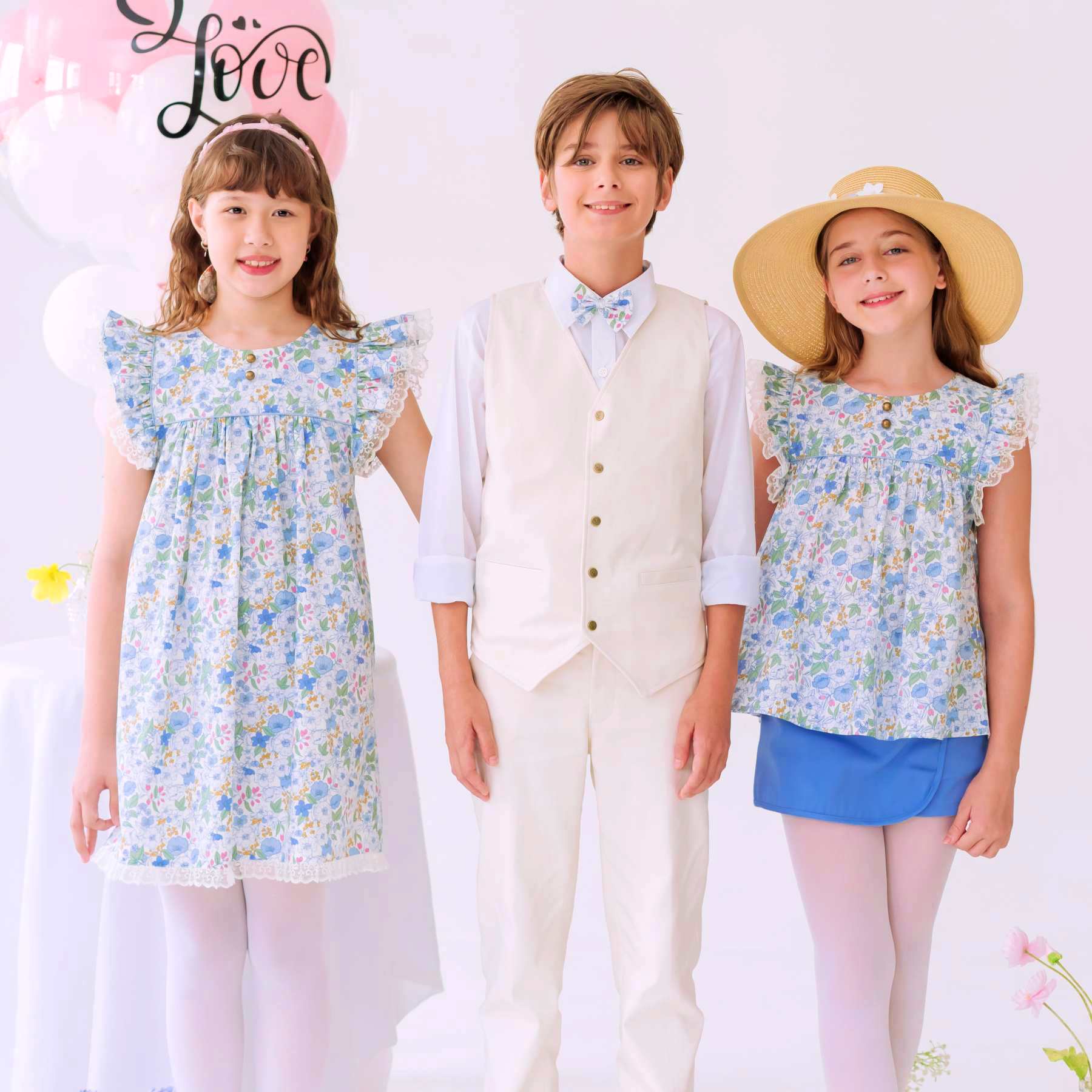 Photo portée de la blouse liberty fille fleurie bleu ciel avec robe liberty bleu ciel Appoline et garçon en costume beige avec noeud papillon liberty bleu ciel. Disponible du 2 au 16 ans pour tout le cortège.