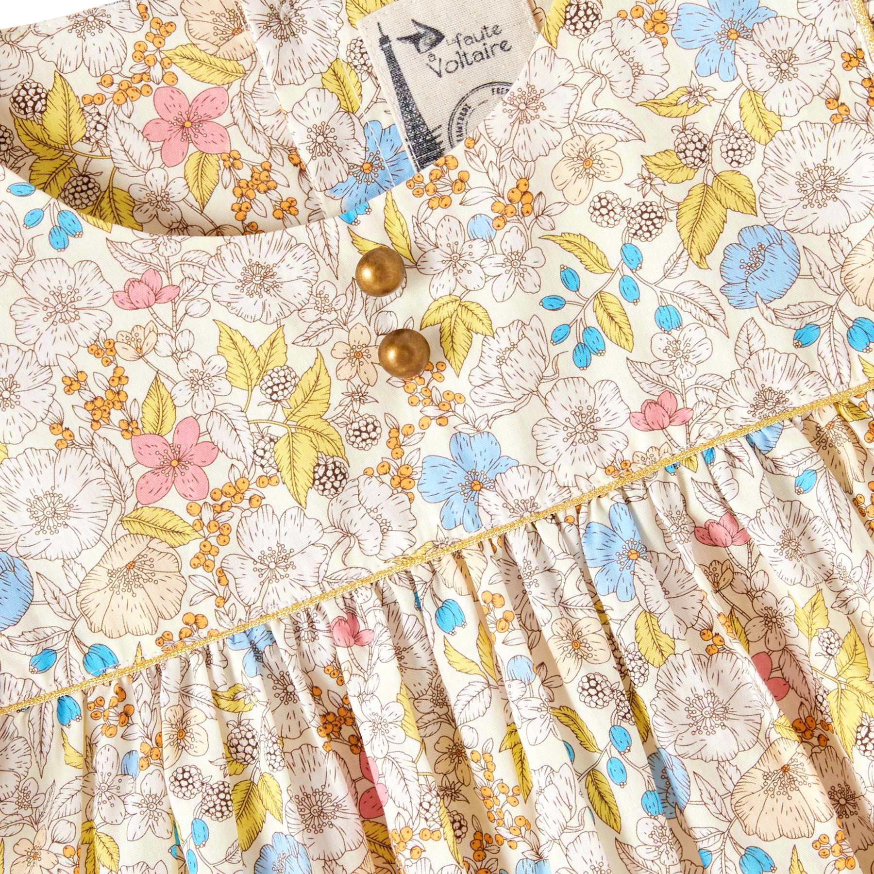 Photo packshot gros plan de la blouse liberty fille jaune, rose, bleu pastel à col rond, biais doré et petits boutons ronds cuivrés décoratif. Nouvelle collection été mode enfant La Faute à Voltaire. Modèle Appoline fleurie jaune Appoline.