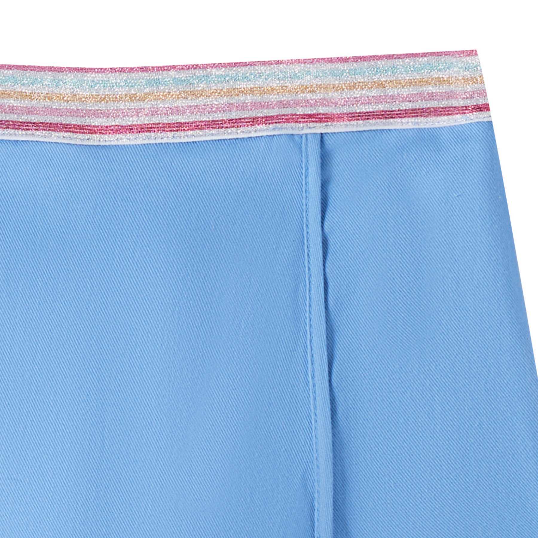 Photo packshot gros plan de la jupe short bleu ciel fille avec coupe portefeuille sur le devant. Taille élastique dans le dos. Ceinture fantaisie à fines rayures multicolores. Modèle disponible du 2 au 16 ans. Taille plutôt petit. Optez pour la taille supérerieure si l'enfant est entre deux tailles ou de morphologie un peu ronde.