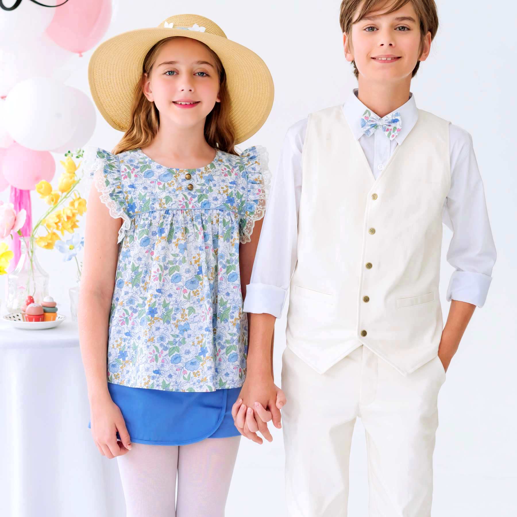 Photo portée de la jupe short bleu ciel fille avec coupe portefeuille sur le devant. Portée avec la blouse liberty fleuri bleu ciel, cette tenue est idéale en tenue de cérémonie. ici avec la tenue costume de mariage beige pour garçon.